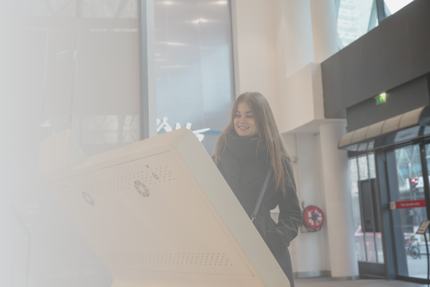 Woman smiling while using an interactive digital wayfinding kiosk in a modern indoor space.