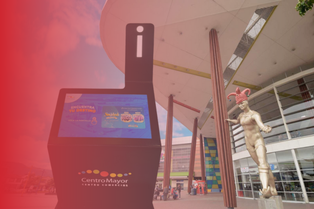 Tótem de orientación digital de ViaDirect frente a la entrada principal del Centro Comercial Centro Mayor en Bogotá, con interfaz interactiva visible y escultura icónica al fondo.