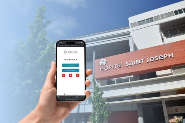 Hand holding a smartphone displaying ViaDirect Mobile Map in front of Hôpital Saint-Joseph in Paris, helping patients and visitors navigate the hospital.