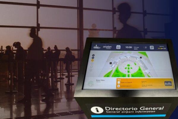 Interactive digital wayfinding kiosk at an airport terminal displaying a real-time indoor map, with passengers in the background.