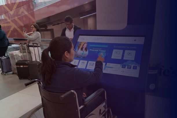 Passenger using an accessible interactive wayfinding kiosk at an airport while seated in a wheelchair.