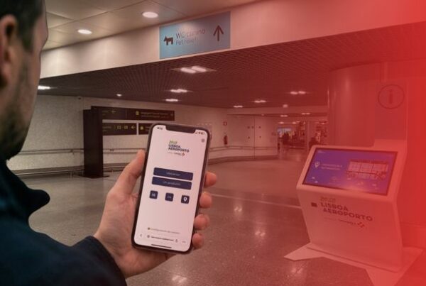 Traveler using a mobile wayfinding map inside Lisbon Airport, with an interactive wayfinding kiosk visible in the terminal.